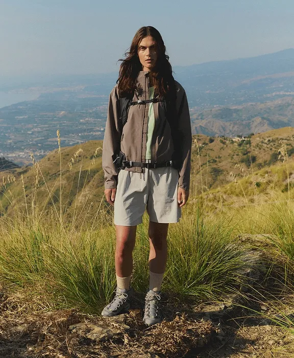 Eine Frau in Wanderbekleidung steht mit Rucksack vor einer weiten Hügellandschaft.